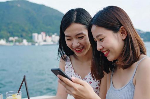 スマホを見ながら会話を楽しむ女子大生 スマホを見ながら会話を楽しむ女子大生の写真