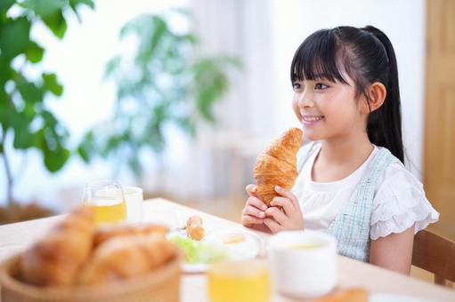 クロワッサンを手に朝食を楽しむ女の子の写真