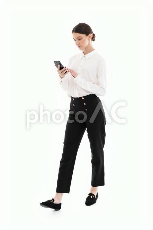 スマホを見ながら歩く白シャツの女性 女性,スマートフォン,持つの写真素材