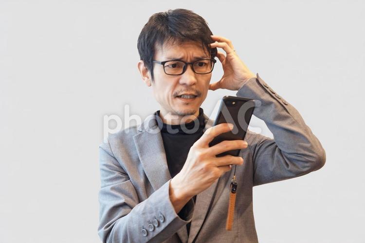 スマホを見て頭を抱える男性 男性,悩む,困るの写真素材