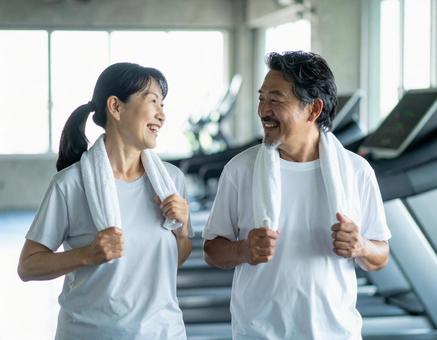 ジムで笑顔で運動する仲良しシニア夫婦 ジムで笑顔で運動する仲良しシニア夫婦の写真
