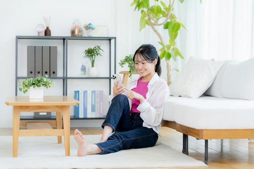 部屋でスマホを操作する若い女性 スマホ,笑顔,若い女性の写真素材