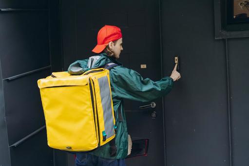 インターホンを押すフードデリバリーの男性の後ろ姿の写真