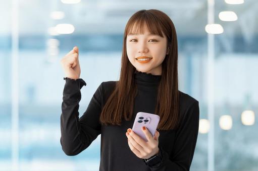 スマホを持ってガッツポーズをする女性 スマホを持ってガッツポーズをする女性の写真