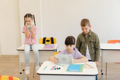 机に座ったりしてタブレットや携帯を見る生徒 男の子,女の子,子どもの写真素材