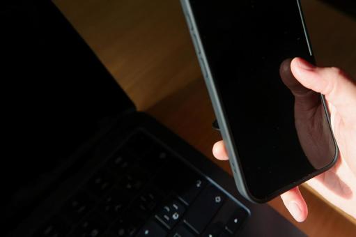 パソコンの前でスマホを操作する男性の手元 スマートフォン,スマホ,携帯電話の写真素材