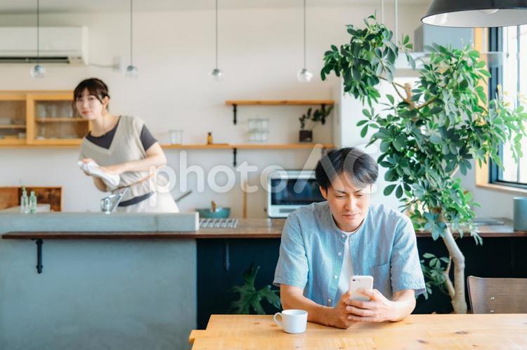 家事をしながら男性を見て怒る女性 スマホ,ゲーム,ギャンブルの写真素材