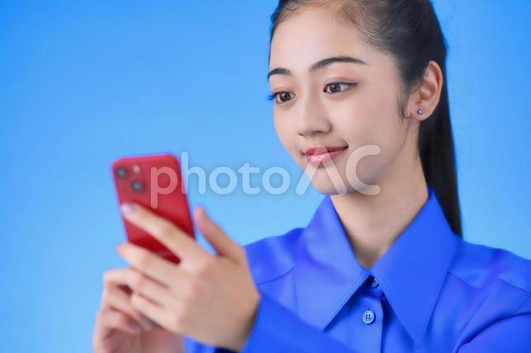 青色背景でスマホを使う女性 女性,日本人,ポートレートの写真素材