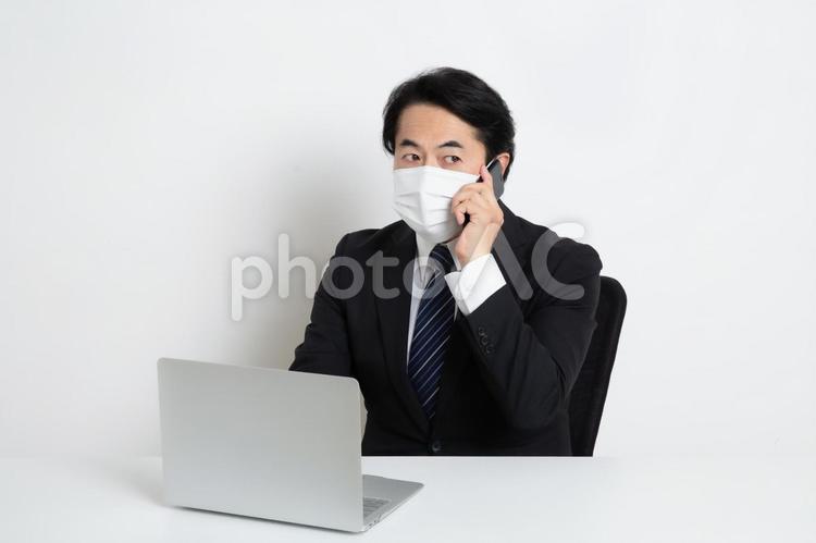 マスクをしながら電話をしている中年のサラリーマン男性 中年,上司,会社員の写真素材