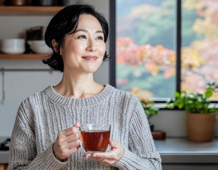 キッチンで紅茶を持ち微笑む女性 キッチンで紅茶を持ち微笑む女性の写真
