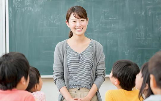 黒板の前に立つ若い女性の小学校教諭 黒板の前に立つ若い女性の小学校教諭の写真