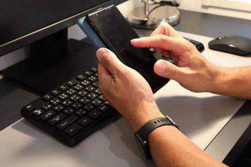 パソコン前でスマホを操作する男性の手元 パソコン前でスマホを操作する男性の手元 パソコン,スマホ,男性の写真素材