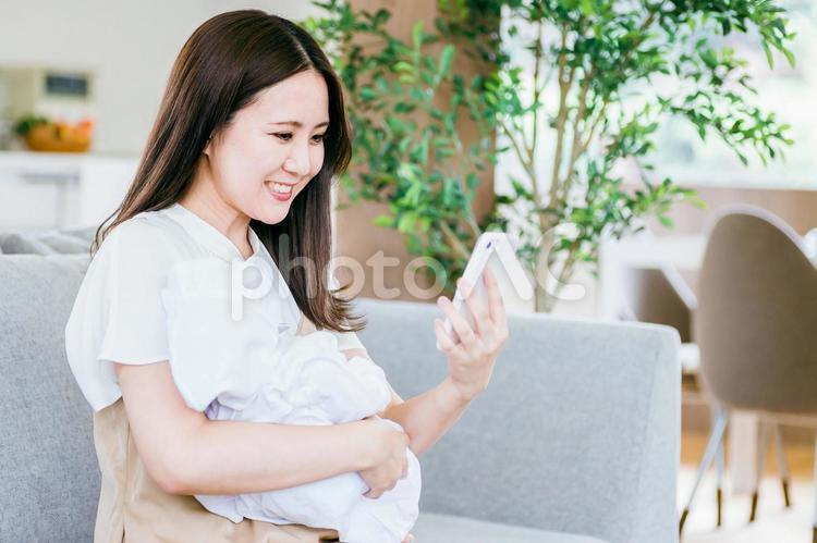 赤ちゃんを抱きながらスマホを使う女性 赤ちゃん,ママ,子育ての写真素材