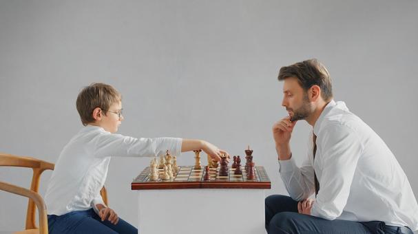 向かい合ってチェスをしているお父さんと男の子(グレー背景) 向かい合ってチェスをしているお父さんと男の子(グレー背景) チェス,親子,お父さんの写真素材