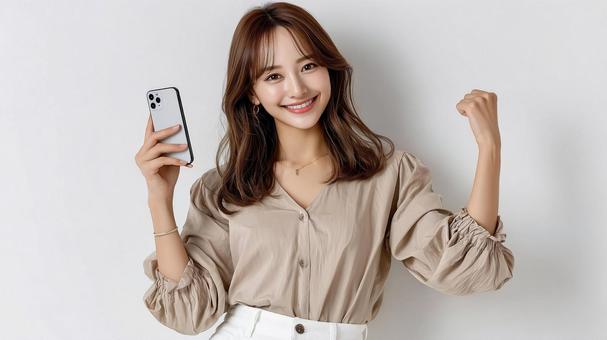 スマホを手に笑顔でガッツポーズする女性 スマホを手に笑顔でガッツポーズする女性の写真