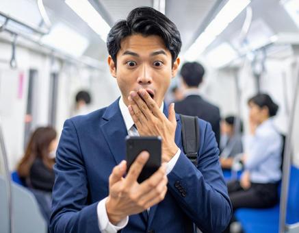 通勤電車でスマホを見て驚く男性 通勤電車でスマホを見て驚く男性の写真