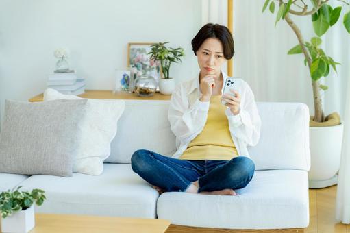 部屋でスマホを使うミドル女性 部屋でスマホを使うミドル女性 スマホ,悩む,困るの写真素材