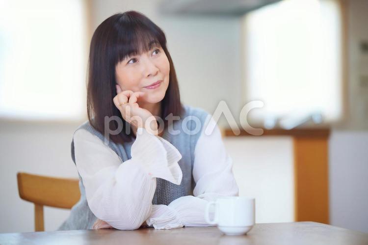 マグカップを置いてテーブルで頬杖をつく女性 女性,日本人,50代の写真素材