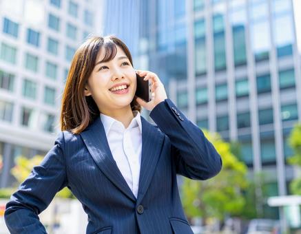 街中で電話をかける若い女性社員の写真