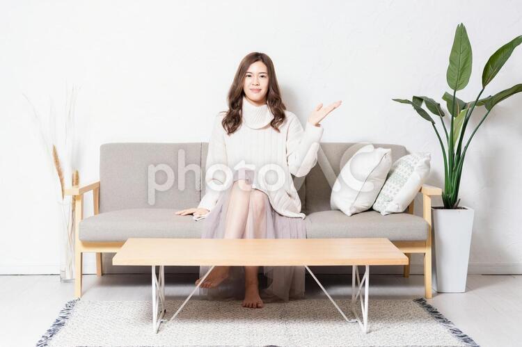 リビングのソファに座って案内のジェスチャーをする若い女性 女性,リビング,座るの写真素材