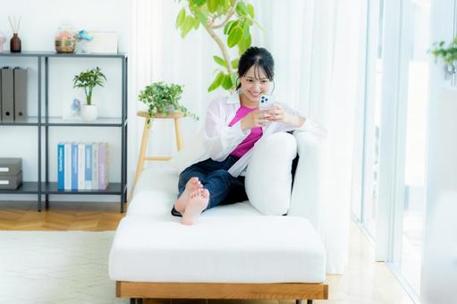 部屋でスマホを操作する若い女性 スマホ,笑顔,若い女性の写真素材