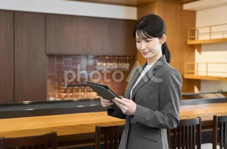 飲食店でタブレットを見るスーツを着た女性 飲食店,女性,スーツの写真素材
