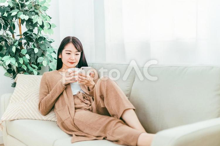 ソファでスマホを使う女性（真顔） スマホ,スマートフォン,ソファの写真素材
