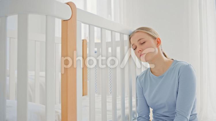 ベッドの柵に頭を付け眠る女性 女性,育児疲れ,眠るの写真素材