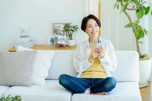 部屋でスマホを使うミドル女性 部屋でスマホを使うミドル女性 スマホ,笑顔,女性の写真素材