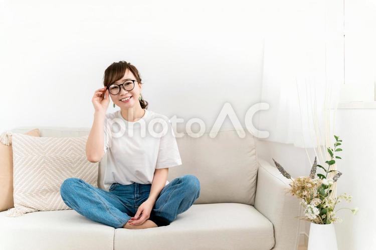 家のソファに座るデニム姿のおしゃれな女性 メガネ,眼鏡,女性の写真素材
