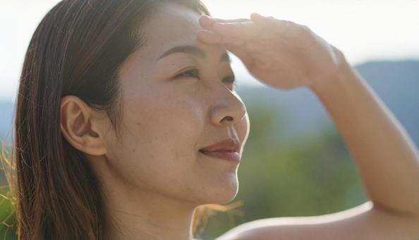 太陽の光をまぶしそうに浴びる女性 太陽の光をまぶしそうに浴びる女性の写真