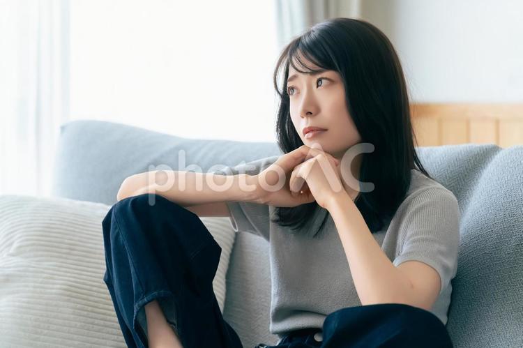 ソファに座って考えごとをする女性 女性,考える,困るの写真素材