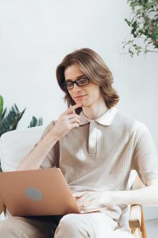 リビングで顎を触りながらノートパソコンを見ている若い男性 男性,外国人,欧米人の写真素材