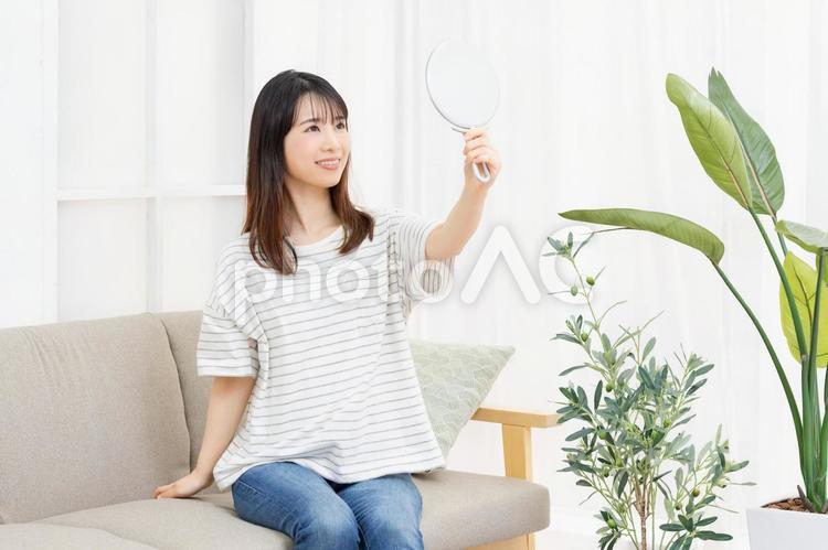 部屋のソファに座って手鏡を使う若い女性 女性,家,ソファの写真素材
