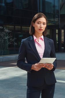 オフィスビルの外でアジア人ビジネスウーマンがタブレットを持って立っている ビジネスウーマン,ビジネス,女性の写真素材