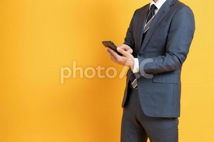 スマホを持つビジネスマン（顔なし） 30代,40代,オレンジバックの写真素材