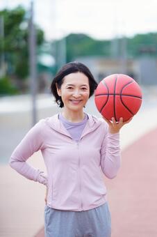 片手でバスケットボールを持ち微笑む女性 女性,バスケットボール,趣味の写真素材
