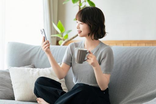 ソファに座ってスマホを使う笑顔の女性 ソファに座ってスマホを使う笑顔の女性の写真