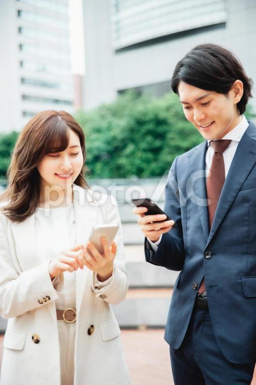 スマホを持って話をするスーツ姿の男女 スマートフォン,アプリ,snsの写真素材