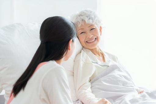 寝ているシニア女性を介護をする介護士 寝ているシニア女性を介護をする介護士の写真