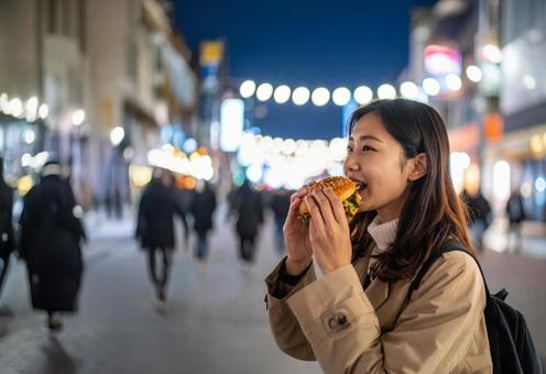 夜のビジネス街でハンバーガーを食べる女子 夜のビジネス街でハンバーガーを食べる女子の写真