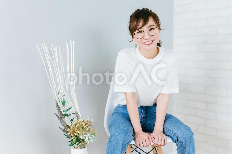 部屋で椅子に座るメガネをかけた日本人女性 メガネ,デニム,眼鏡の写真素材