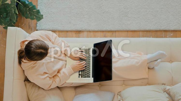 ソファーに足を伸ばして座ってパソコンをする女性 女性,ポニーテール,足を伸ばすの写真素材