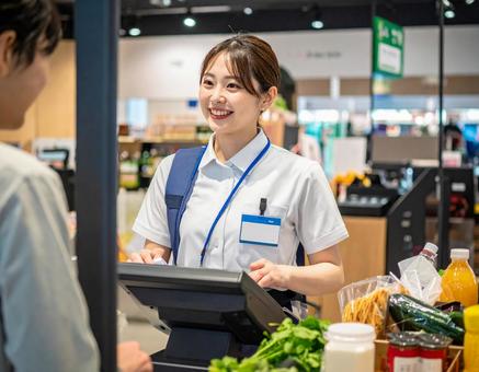 スーパーで笑顔でレジ業務をする女性店員 スーパーで笑顔でレジ業務をする女性店員の写真