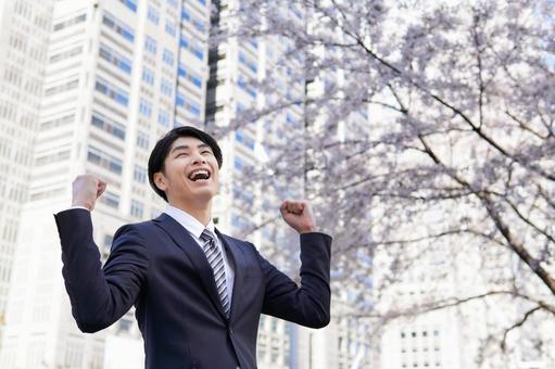 Japanese male businessman doing guts pose against the background of cherry blossoms in the office district, ein mann, ein geschäftsmann, neuer mitarbeiter, JPG