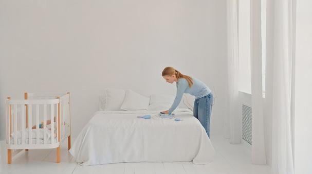 ベッドの上でベビー服を畳む女性 ベッドの上でベビー服を畳む女性 女性,横向き,横顔の写真素材