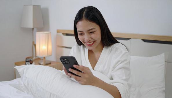 ベッドルームでスマホを見る日本人女性 ベッドルームでスマホを見る日本人女性の写真