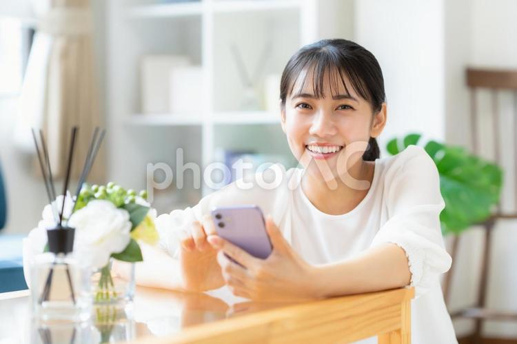 リビングでスマホを見る大学生の女性 女性,スマホ,大学生の写真素材