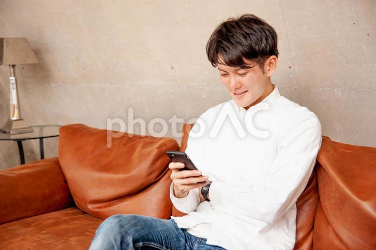 スマホを見て部屋で過ごす男性 スマホ,男性,笑顔の写真素材