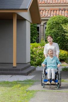 庭で車椅子に乗るシニア女性とヘルパー 庭で車椅子に乗るシニア女性とヘルパーの写真